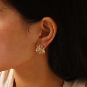Détail de boucles d'oreilles cubes dorées avec zircons portées sur l'oreille
