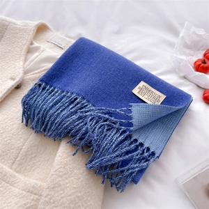 Detail of blue cashmere-like scarf with fringe and beige brand label on white plush coat