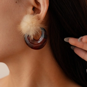 Detail of earring with beige pom-pom and amber resin hoop on a female model