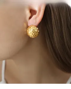 Detailed view of gold ball earrings with hammered texture on a model's ear