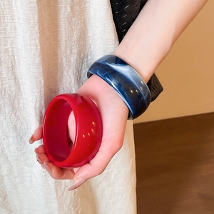 Close-up of model wearing vibrant red and marbled blue acrylic bangles on a white background