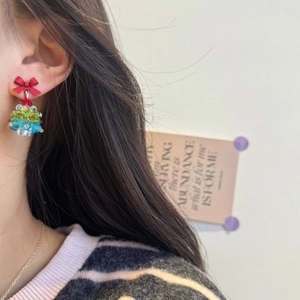 Close-up of handmade beaded Christmas tree earrings with a red bow on a female model