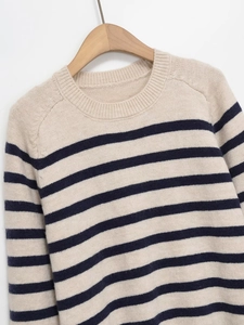 Close-up of the ribbed crew neck and navy blue stripes on the off-white knit sweater