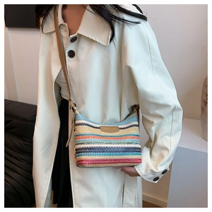 Detail view of rainbow striped woven crossbody bag worn by a model in soft studio lighting