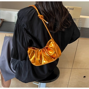 Shiny orange-gold metallic pleated cloud bag shown on a model for a stylish underarm look