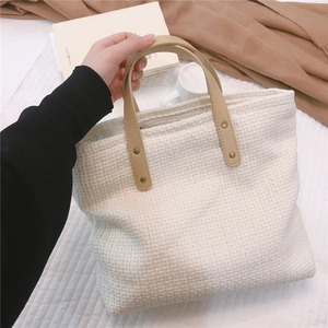 Close-up of woven tote bag with khaki leather handles and golden rivet accents