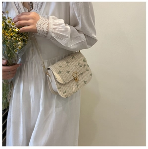 Detail of floral embroidery and gold metal clasp on woven cream crossbody bag