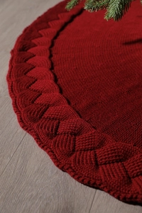 Close-up of deep red knitted Christmas tree skirt featuring detailed cable knit patterns
