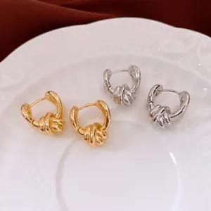 Chic twisted knot gold and silver hoop earrings on a vintage ceramic plate background