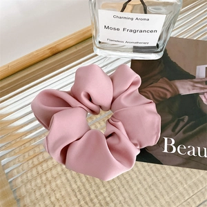 Macro detail of a large pink satin scrunchie on a glass tray for elegant hair styling