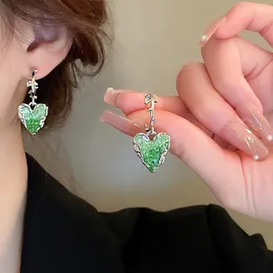 Detail of heart-shaped earrings with green crystal inlay and silver thorn-style hooks