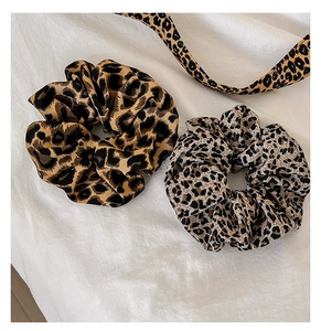 Flat lay detail of brown and black leopard print scrunchies on white fabric texture