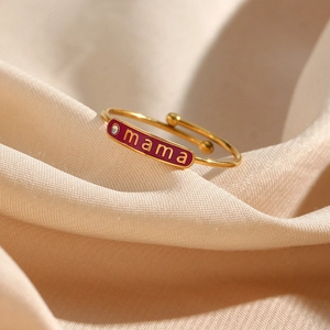 Close-up of golden adjustable ring with red enamel MAMA plate and clear gemstone