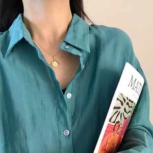 Close-up of gold hexagonal coin pendant necklace worn with a deep green shirt