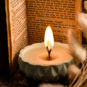 Aromatic teardrop candle in light blue pleated glass jar on vintage book pages