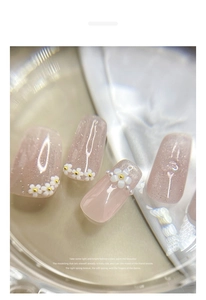 Macro shot of 3D white resin flowers and butterflies on sparkly nude pink press-on nails