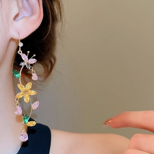 Close-up of dangling zircon flower and butterfly earrings worn on a female ear