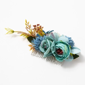 Detailed view of floral hair comb with blue silk flowers and green leaves on white background