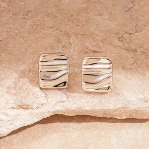 Macro detail of silver geometric earrings with wavy texture on a natural stone background