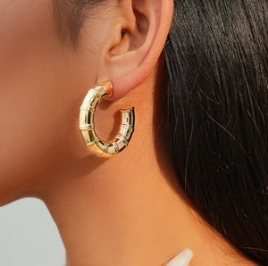 Polished gold bamboo textured C-shape hoop earrings worn by a model in a close-up view