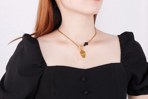 Close-up of golden skull pendant with black cross on model's neck for jewelry display