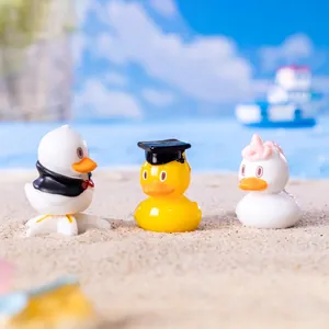 Three mini resin duck figurines in a beach scene featuring graduation and suit themes