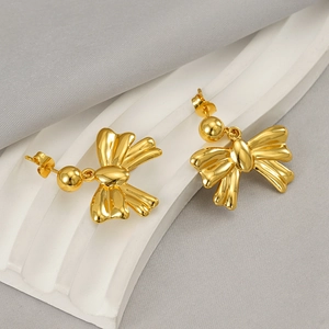 Polished 18K gold plated stainless steel bow stud earrings on a wavy textured display
