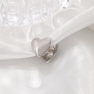Polished silver heart ear clip earring on white silk background with glass decor