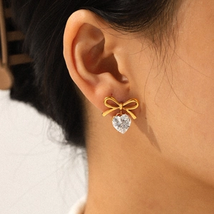 Close-up of golden bow earrings with heart-shaped zircon crystal worn on model ear
