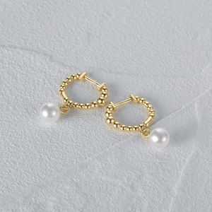 Macro detail of elegant gold hoop earrings with white round pearls on grey stone