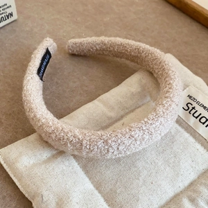 Close-up of a wide beige sherpa headband with a black handmade label on canvas