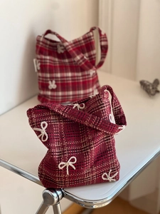 Detail of red plaid tweed tote bag with white bow accents on a minimalist table
