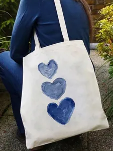White canvas tote bag with blue watercolor heart prints carried on shoulder in garden