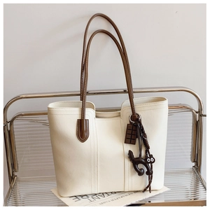 Close-up of cream tote bag with brown leather straps and cute black cat charm on a metal shelf