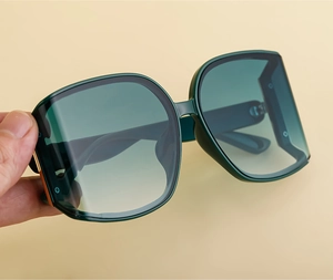Detail of dark green oversized sunglasses with curved lenses held against yellow background