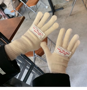 Detail of beige knit gloves with embroidered Vous êtes tout pour moi fabric tag