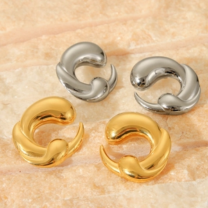 Macro view of chunky 18K gold and silver C-shaped twisted earrings on textured rock