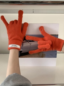 Detail of bright orange knitted gloves with ribbed cuffs and branded fabric label