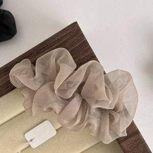 Detail of a beige tulle scrunchie with soft pleats on a wooden tray with a white tag