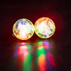 Macro view of glowing disco ball earrings with colorful light reflections on black surface
