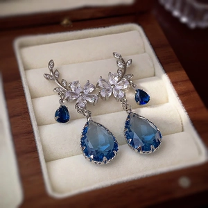 Macro shot of silver floral earrings with zircon leaves and dark blue pear-cut gemstone