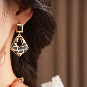 Close-up of geometric earrings with black and white checkered pattern and gold trim