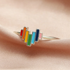 Dettaglio di un anello a cuore in smalto arcobaleno su tessuto satinato rosa