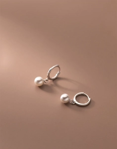 Detail shot of elegant polished stainless steel hoop earrings with glossy white pearls