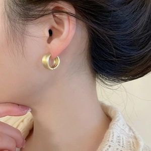 Close-up of matte gold round stud earrings with a brushed texture on model's ear