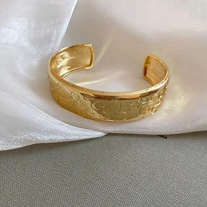 Detailed close-up of golden oval open bangle with vintage floral engraving on white silk