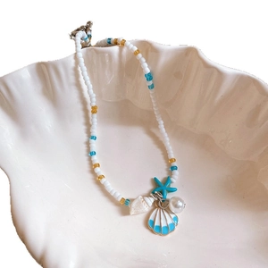 Starfish pearl necklace with blue beads and shells displayed in a white conch shell