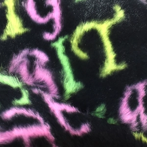 Close-up of thick plush faux fur texture with neon pink and green letter patterns