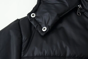 Detail of hood neckline on black padded jacket with metal snap buttons and zipper