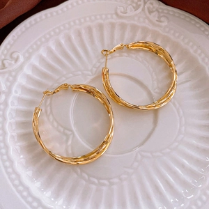 Detailed close-up of golden twisted geometric hoop earrings on a vintage ceramic plate